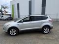 A 2014 Ford Escape in silver parked on a gravel surface with a side view showing its sleek design and alloy wheels