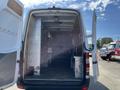 A 2010 Mercedes-Benz Sprinter with its rear doors open revealing an empty cargo space featuring metal shelving along the sides