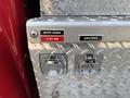 A metal panel on a 1999 Freightliner FL80 with labels for a battery charger and block heater featuring two connection ports and a textured diamond plate surface