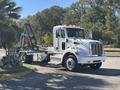 A 2020 Peterbilt 330 truck with a white body and chrome accents featuring a flatbed and a hydraulic arm for loading and unloading materials