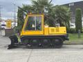 A yellow 2004 Bombardier SW48 snow groomer with a plow attachment and tracks designed for snowy terrain