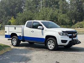 A white 2017 Chevrolet Colorado with a blue stripe and utility bed attachment, positioned at a slight angle showcasing its front and side features