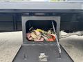 A storage compartment under a 2018 Ford F-750 truck containing various straps in different colors and a chain attached to the compartment door