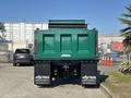 A green 2015 Peterbilt 337 truck is shown from the rear with a raised dump bed and visible company branding on the mud flaps
