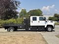 A white 2005 GMC C7500 Topkick truck with a flatbed and black tool box on the side is parked on a driveway
