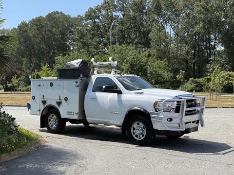 A white 2020 Ram 2500 truck with a custom utility body and tool boxes on the back equipped with a ladder rack and chrome bumpers on a sunny day