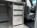 A metallic storage unit with three drawers inside a 2016 GMC Savana van cabinet next to a driver's seat