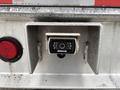A rearview camera mounted in a metal bracket with red lights on either side and a weathered surface
