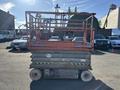 A red and gray 2010 SkyJack SJ 4626 scissor lift with a raised platform and safety rails
