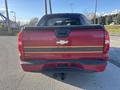 A red 2011 Chevrolet Avalanche with a black bed cover and a gold stripe running along the side, showing the rear view with a Chevrolet emblem visible on the tailgate