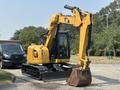 A 2018 Caterpillar 308E2 excavator with a yellow exterior and a bucket attachment is positioned on a gravel surface ready for operation