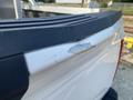 Close-up of a dent and paint damage on the tailgate of a white 2016 Ford F-150