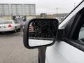 A 2019 Ford Explorer's side mirror with raindrops on the surface reflecting a hand holding a smartphone