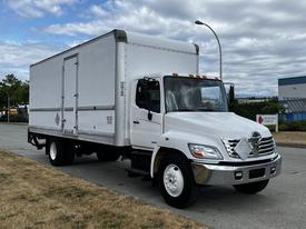A white 2006 Hino 268 box truck with a large cargo area and a single cab is parked on the street