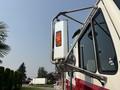 A close-up view of a 1999 Freightliner FL80's side mirror with an orange indicator light mounted on a chrome arm