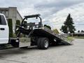 A 2022 Ford F600 tow truck with a flatbed tilted towards the ground and a light bar on top