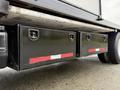 A black storage box with a reflective strip attached to the side of a 2007 GMC F7500 truck located beneath the vehicle's bed