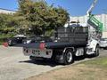 A 2020 Peterbilt 330 flatbed truck with a black cargo bed and a sturdy rear bumper parked in a lot with trees and vehicles in the background