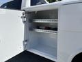 A white truck door is open revealing an empty storage compartment with two metal shelves and some equipment on the floor
