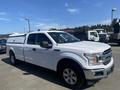 A white 2019 Ford F-150 with a fitted truck cap parked at a dealership showcasing its sleek design and modern features