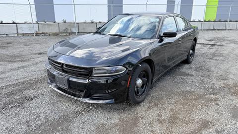 A black 2015 Dodge Charger with a sleek design featuring a sporty front grille and round headlights parked on gravel