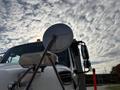 A silver side mirror reflecting a cloudy sky mounted on a white 2013 Freightliner 114SD truck
