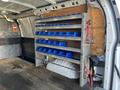 Interior of a 2016 GMC Savana van featuring shelves with blue storage bins mounted on the wall and a flat floor with visible wooden planks