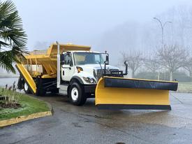 A 2016 International 7400 plow truck with a yellow snow plow attached to the front and a large yellow salt spreader in the back