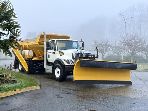A 2016 International 7400 plow truck with a yellow snow plow attached to the front and a large yellow salt spreader in the back