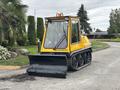 A yellow 2004 Bombardier SW48 snowplow with a front blade and rubber tracks is parked on a paved surface
