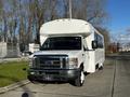 A 2014 Ford Econoline bus with a sleek white exterior and large windshield is parked, featuring a prominent front grille and ample passenger space inside