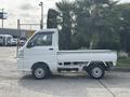 A white 2010 Daihatsu Hijet mini truck is parked, featuring a flatbed design with a compact body and round headlights