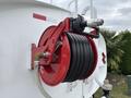 A red hose reel mounted on a white surface with a hose coiled inside and a metal nozzle attached to the reel