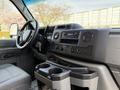 The interior dashboard of a 2023 Ford E-450 featuring controls for audio and climate along with cup holders and a gear shift