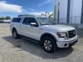 A silver 2014 Ford F-150 pickup truck with a camper shell and off-road tires parked with its driver side facing the viewer