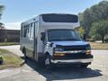 A 2020 Chevrolet Express shuttle bus with a silver body and black front features large windows and side mirrors parked in a spacious area