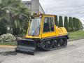 A yellow 2004 Bombardier SW48 snowcat with tracks and a front-mounted snow plow positioned on a paved surface