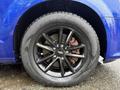 Close-up of a black alloy wheel with a shiny finish and visible brake calipers on a blue Dodge Grand Caravan with water droplets on the surface