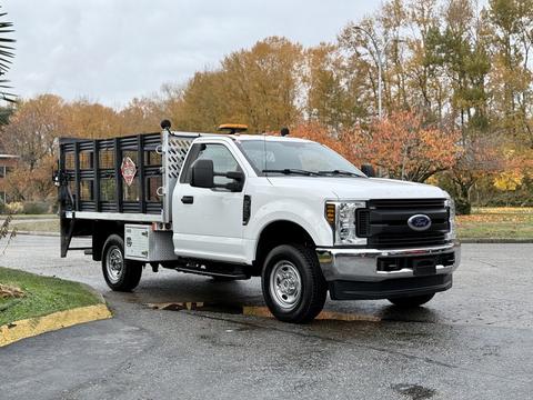 A white 2019 Ford F-350 SD pickup truck with a flatbed and a safety railing on the back parked on a paved surface