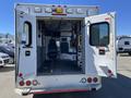 A 2013 Chevrolet Express ambulance with open rear doors revealing an empty interior featuring a driver’s seat and medical equipment storage.