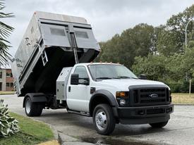 A 2008 Ford F-450 Super Duty truck with a raised dump bed and a white exterior parked on a concrete surface