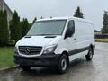 A 2016 Mercedes-Benz Sprinter van with a white exterior and black accents parked on a wet driveway