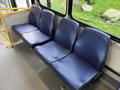 A row of three blue vinyl bus seats with a textured surface and no seatbelts