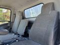 The interior of a 2022 Isuzu NQR featuring two gray patterned seats designed for a commercial truck with adjustable seat belts and a driver’s cockpit area