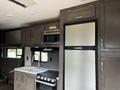 Interior view of a 2021 Jayco Jay Flight featuring a kitchen area with a microwave stove and refrigerator along with wooden cabinetry and a sink