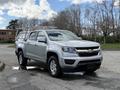 A 2018 Chevrolet Colorado pickup truck with a silver exterior parked on a street featuring a utility bed cap and alloy wheels