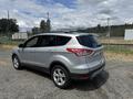A silver 2015 Ford Escape parked on gravel with its rear and side visible showing a sleek design and modern features