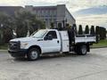 A white 2015 Ford F-350 with a flatbed and a mounted lift gate is parked, showcasing its utility design and functionality