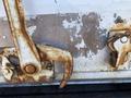 Close-up of rusted metal latch and hook on a vehicle's rear door showing peeling paint and corrosion