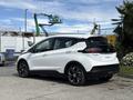 A white 2023 Chevrolet Bolt EV with a sleek design and modern features is parked at an industrial location showcasing its rear and side profile